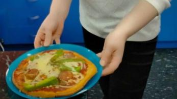 Young person presents pizza with healthy toppings.