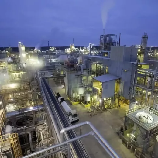 One of Albemarle's two manufacturing plants in Magnolia Arkansas is pictured at dusk, with multiple structures, pipes, and storage tanks illuminated by artificial lights. Steam or smoke rises from various sections, giving a sense of ongoing operations. The sky is deep blue, indicating early evening.